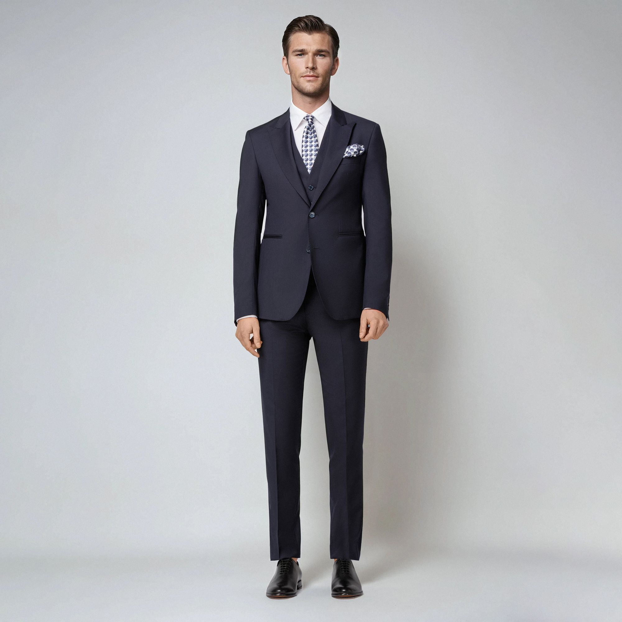 Elio Evan three-piece navy blue suit with peak lapels and golden emblem. Slim Bristol fit. Made in Italy.