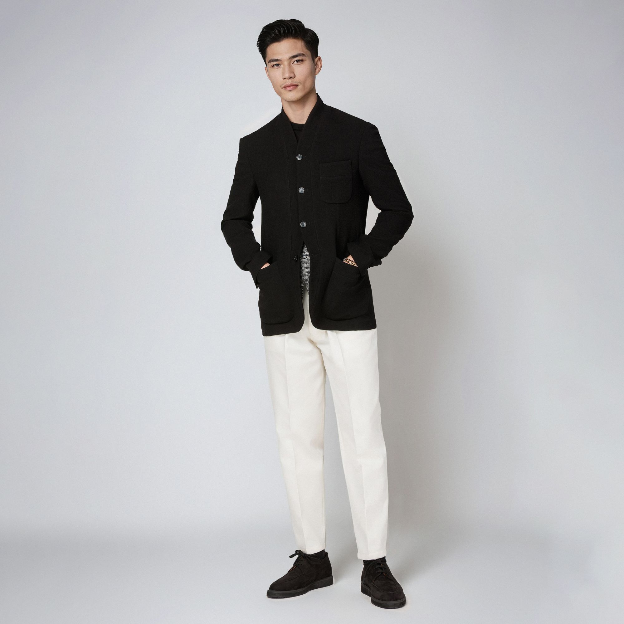 Man wearing an Elio Evan total look with a black minimal wool jacket and white trousers.